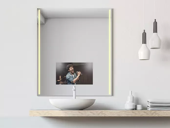 A man singing displayed on a mid-warm lighted mirror TV above a lone basin.