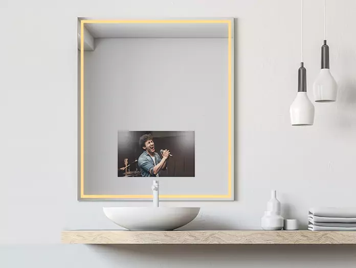 A man singing shows on the screen of a warm-lighted mirror TV above a single sink.