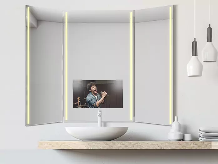 A mid-warm, lighted trifold mirror TV shows a man singing, placed above a single washbowl.
