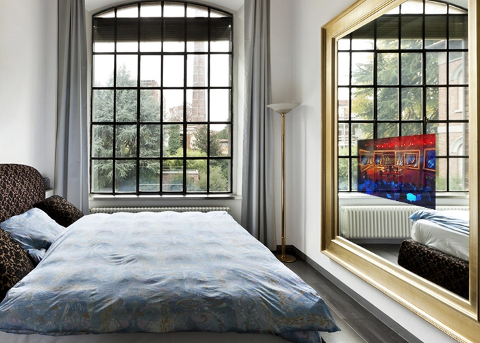 Dormitorio tamaño king en una habitación de hotel con una amplia ventana de vidrio y una TV espejo única en Santiago.