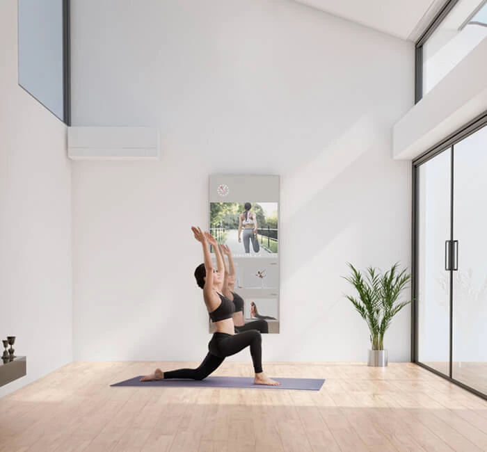 A woman exercises as she watches a video on her fitness mirror in a modern room.