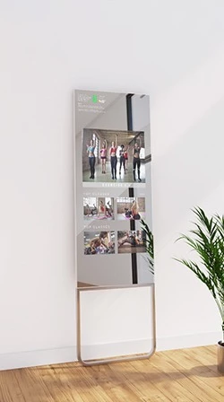 A white wall displays the fitness mirror in a lean on mount design, showing videos for exercising.