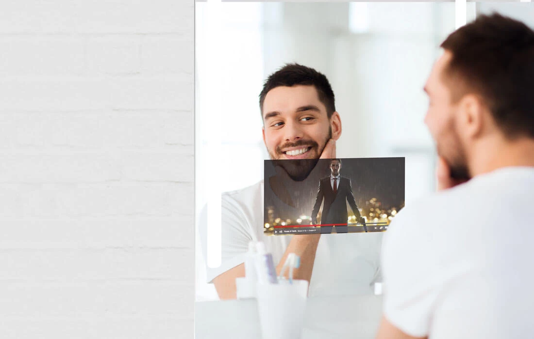 A man watching a movie while looking at his reflection on a smart mirror.
