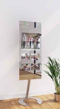 A white wall displays the fitness mirror in stand alone mount design, showing videos for exercising.
