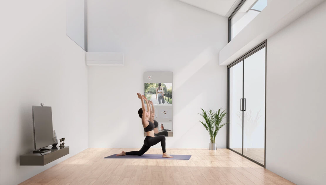 A woman practicing yoga in a contemporary tidy room while using her fitness mirror TV.