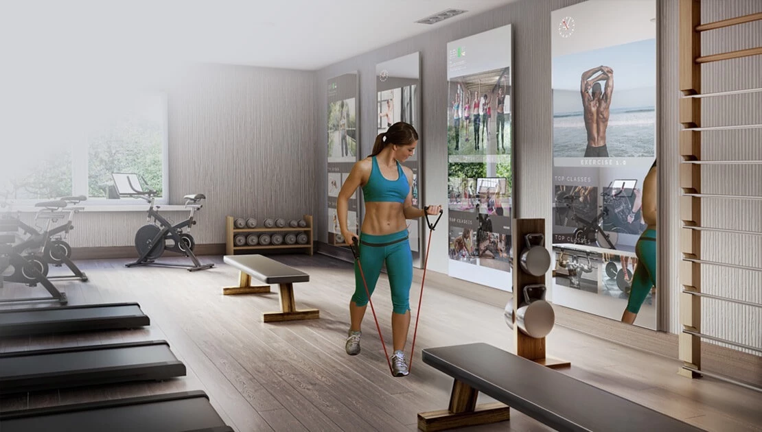 An elegant well equipped gym with a woman working out using an intelligent fitness mirror.