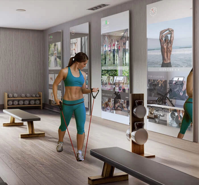 A woman working out using gym equipment in a gym while she uses her fitness mirror TV.